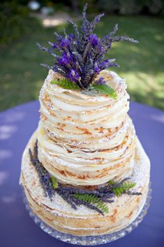 a wedding cake with lavender flowers on top is sitting on a blue tablecloth in the grass