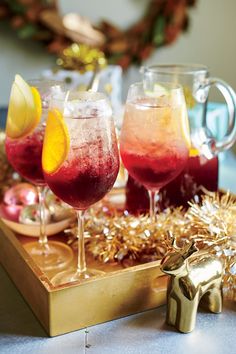 three glasses filled with different colored drinks on top of a wooden tray next to gold tinsel