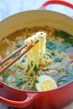 a person holding chopsticks over a bowl of noodles and vegetables with broth