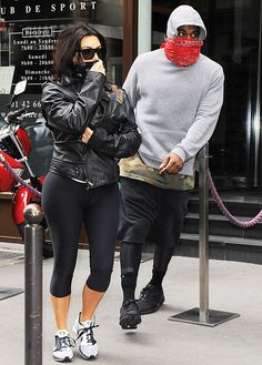 the man and woman are walking down the street talking on their cell phones while wearing masks