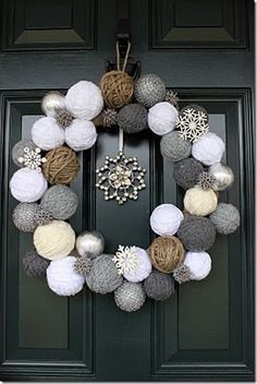 a wreath made out of yarn and balls is hanging on the front door with snowflakes