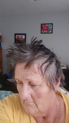 an older woman with gray hair and yellow shirt looking at her cell phone while sitting in bed