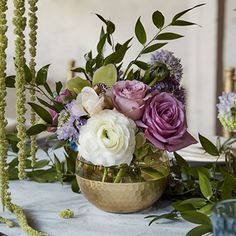 an arrangement of flowers in a gold bowl on a table with greenery and candles