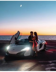 two people sitting on the hood of a white sports car with their hands in the open doors