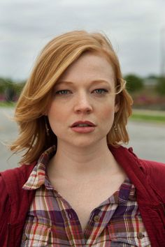 a close up of a person wearing a red jacket and plaid shirt with her eyes closed