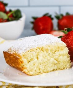 a piece of cake with powdered sugar on top and strawberries in the background