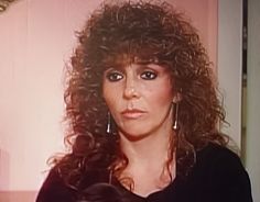 a woman with long curly hair wearing earrings and black shirt in front of a mirror