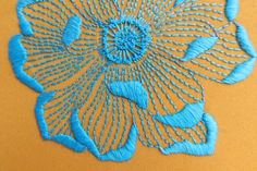 a close up of a blue flower on an orange cloth with stitching in the middle