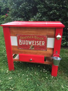 a red wooden budweiser cooler sitting in the grass