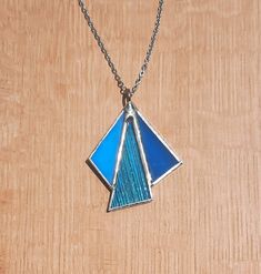 a blue and silver necklace on a wooden surface with a chain hanging from the neck