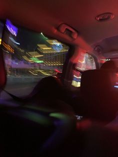 the interior of a car with city lights in the background and buildings lit up at night