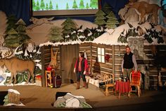 two people standing on stage in front of a christmas scene with deer and snow scenes