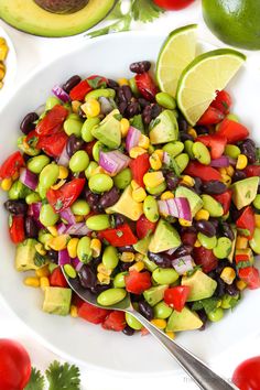 a white plate topped with a salad next to sliced avocados and limes