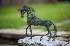 a wire sculpture of a horse on top of a rock in front of some grass