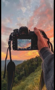 a person holding up a camera with the sun setting in the background