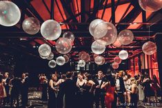 a large group of people standing around in a room filled with white and red balloons