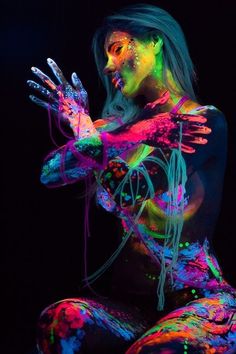 a woman covered in neon paint holding her hands up to her chest and looking at the camera