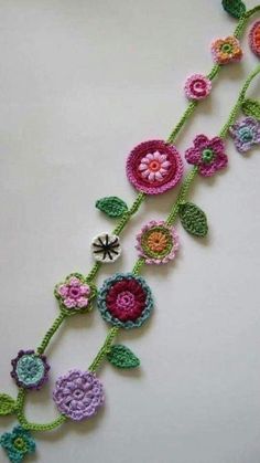 crocheted flowers are arranged on the side of a white tablecloth with green leaves