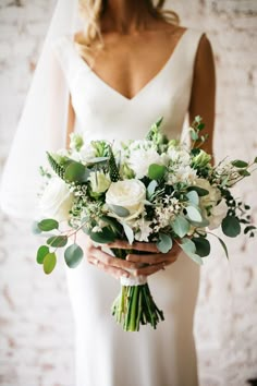 a bride holding a bouquet of white flowers and greenery