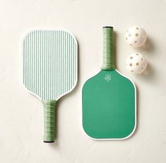 two paddles and three balls on a white surface with a green board next to it