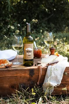 a bottle of wine sitting on top of a wooden box next to two glasses of wine