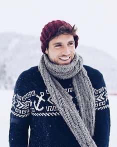 a man wearing a hat and scarf standing in the snow with his hands in his pockets