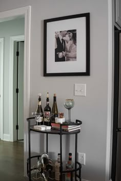 a table with wine glasses and bottles on it in front of a framed photo above