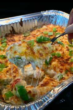 a person is taking a piece of pizza from a foil pan with green onions and cheese