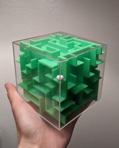 a hand is holding a plastic cube that looks like it has been made out of green squares