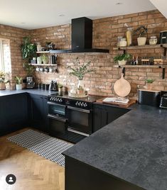 a kitchen with brick walls and black cabinets, an oven, counter tops, and potted plants on shelves