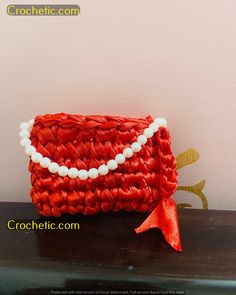 a red purse with pearls on it sitting on top of a wooden table next to a wall