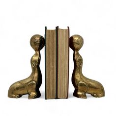 two golden figurines are sitting next to an open book on a white background