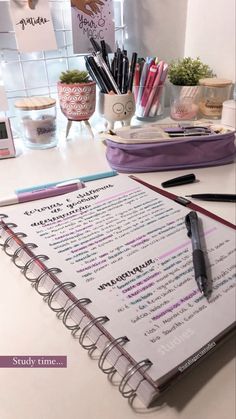 an open notebook sitting on top of a table next to a pen and pencil holder