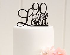 a white cake topped with a black 90th birthday cake topper and pink flowers