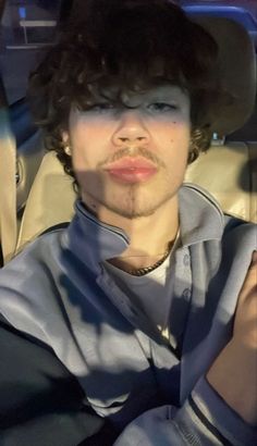 a man with curly hair wearing a hat and sitting in the back seat of a car