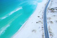 an aerial view of the beach and ocean with a long road going through it's center