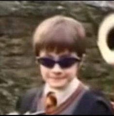 a young boy with sunglasses and a tie holding a large object in front of him