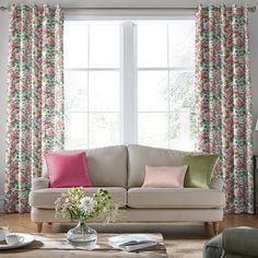 a living room filled with furniture and windows covered in pink flowers on the drapes