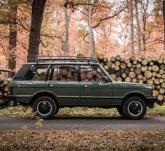 an old car is parked next to a pile of logs