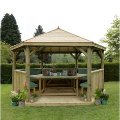 a wooden gazebo sitting in the middle of a lush green field with potted plants