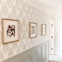 three framed pictures hang on the wall next to a white and gray wallpapered hallway