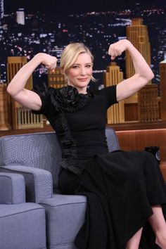 a woman sitting on top of a blue couch in front of a tv screen with her arm raised