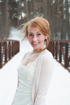 a woman in a white dress standing on snow covered ground with her hair blowing in the wind