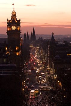 a city street filled with lots of traffic under a clock tower at dusk, as the sun sets