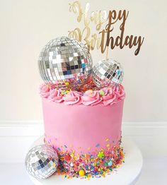 a pink birthday cake with disco balls and confetti on the top is shown