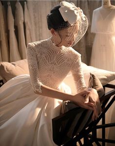 a woman wearing a white dress and veil sitting on a chair in front of mannequins