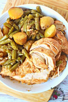 a white plate topped with meat and green beans on top of a wooden cutting board