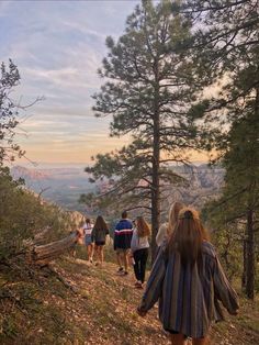 a group of people walking up a hill on a trail in the woods at sunset