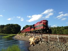 a red train traveling down tracks next to a body of water with trees in the background