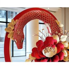 a red and gold dragon sculpture sitting in front of a window next to a flower arrangement